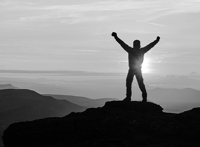 Person with arms raised on a mountain summit at sunrise